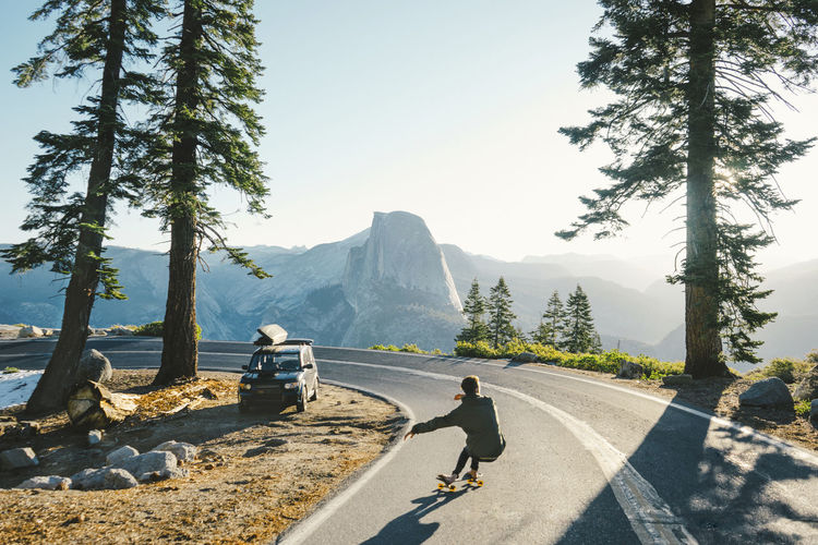 Rear view of man skateboarding on road by mountains against clear sky