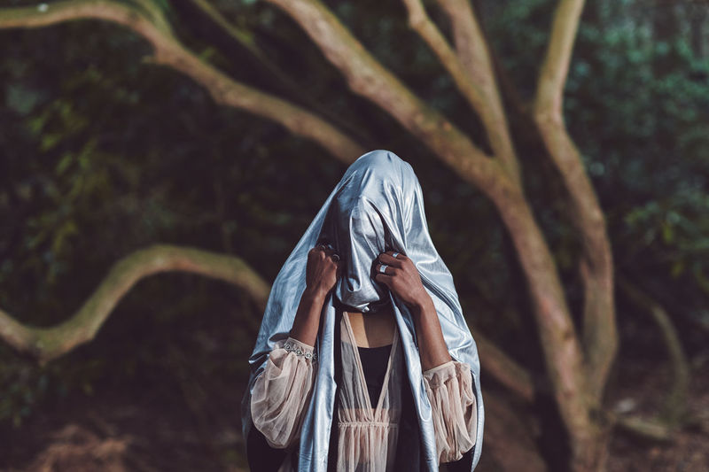 Close-up of woman with textile on face standing against tree