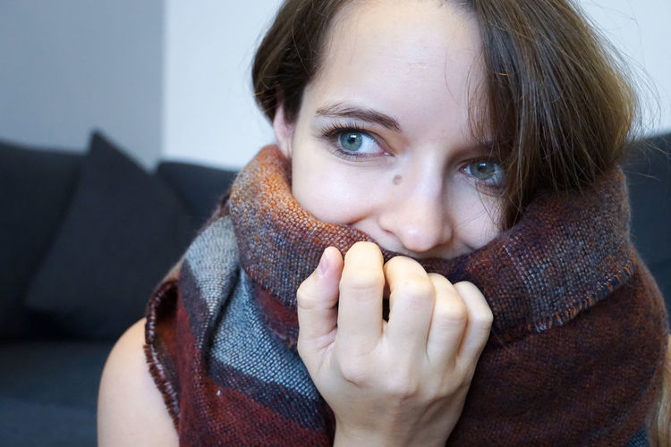 Close-up of woman covering face with scarf sitting on sofa at home