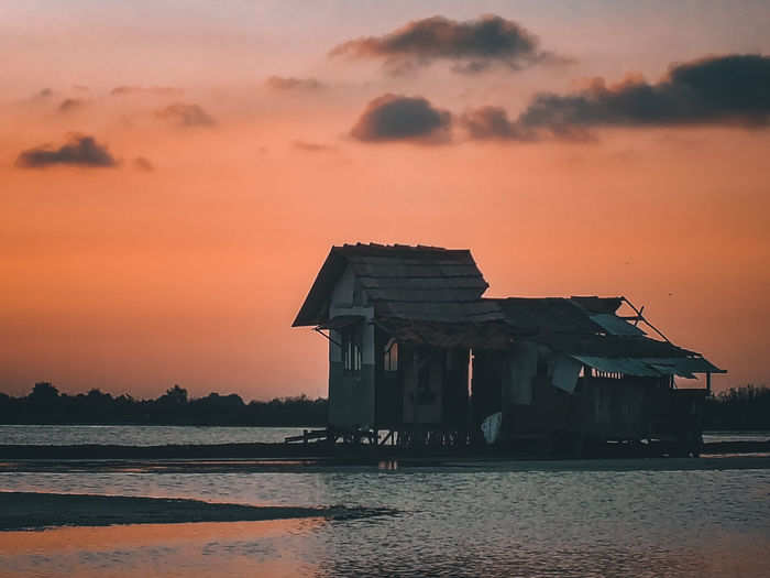 House by sea against orange sky