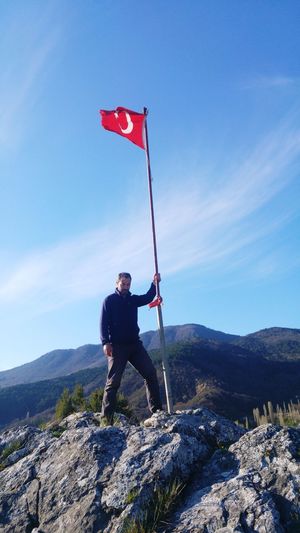 Man standing by turkish flag on mountain against sky