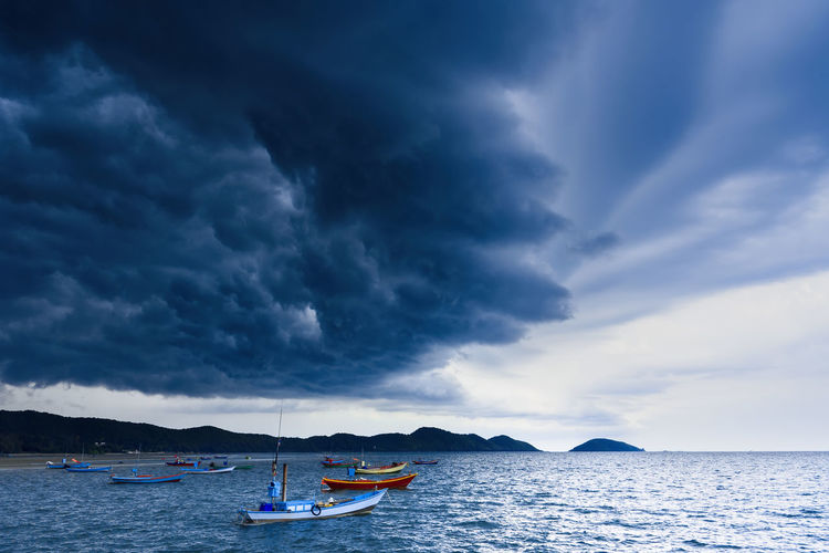 Boats moored on sea against cloudy sky