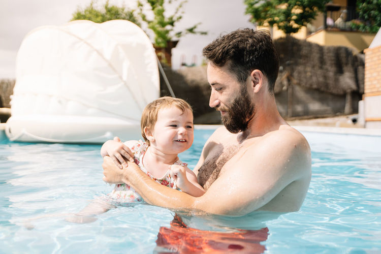 Man inside a house pool with a little girl in his arms swimming