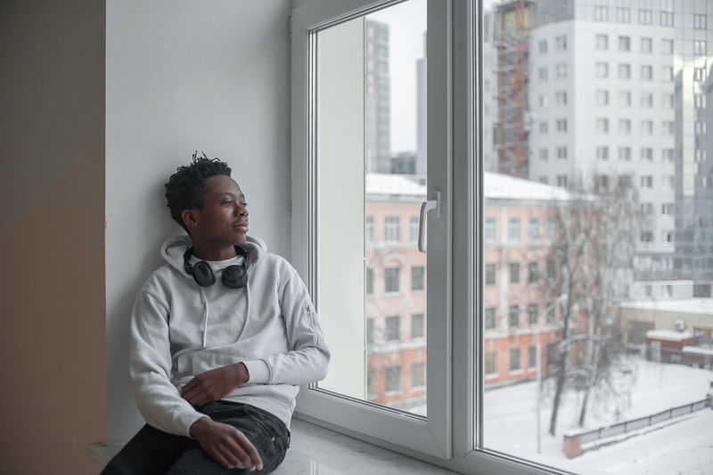 Young male african american student sitting on a windowsill in an educational institution