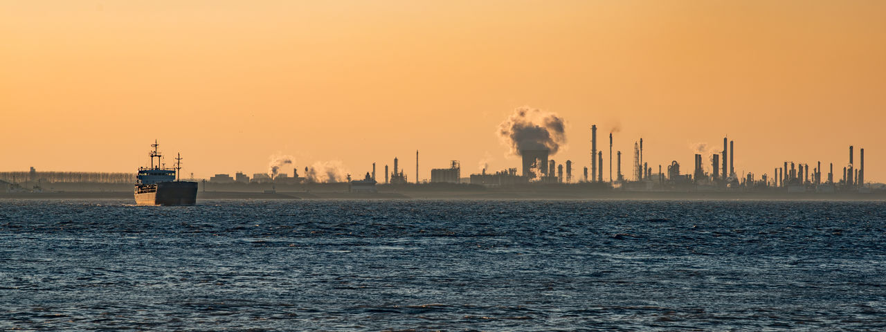 Panoramic view of silhouette factory by sea against clear sky during sunset
