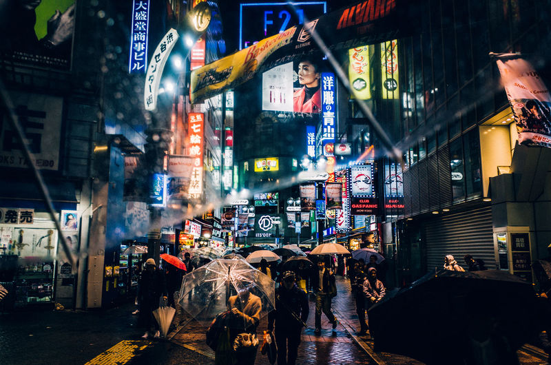People walking on city street with umbrellas in rain during night
