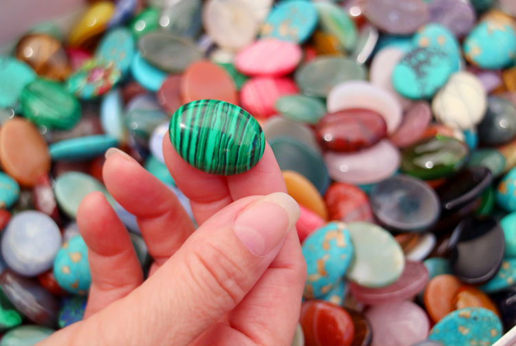Closeup of woman's hand picking a malachite stone with semi precious stones pile in background