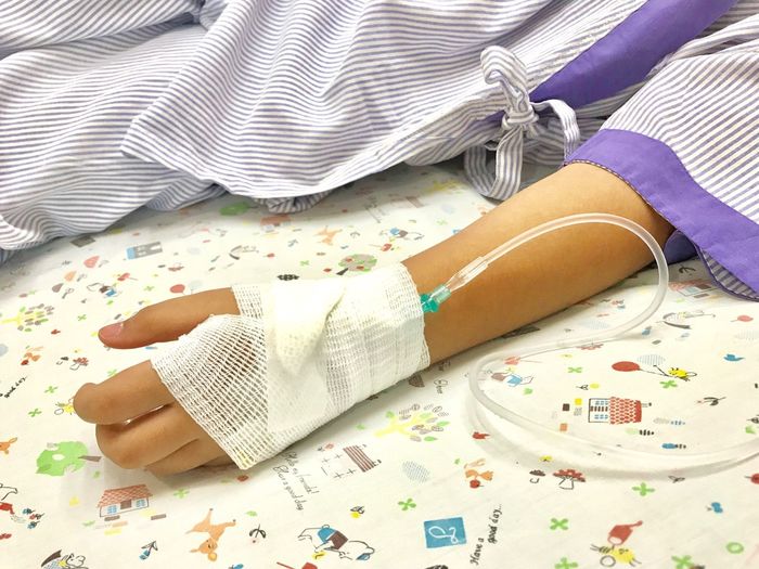 Midsection of woman with iv drip on hand lying in bed