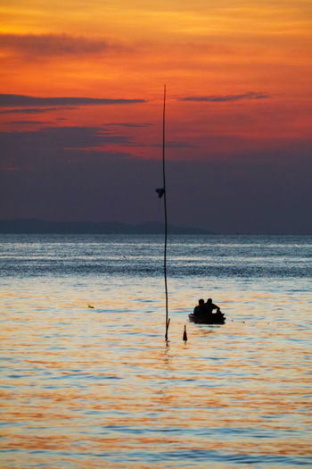 Silhouette fishing rod on sea against sky during sunset