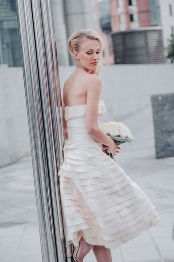 Beautiful bride with bouquet against wall in city