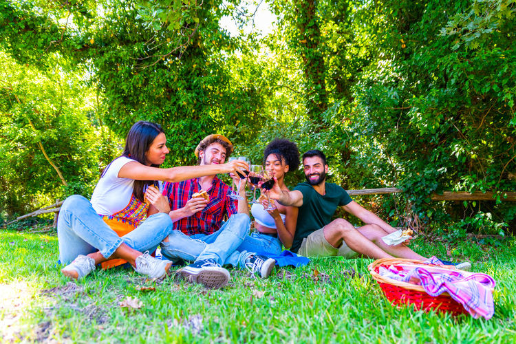 Group of friends sitting on grass against trees