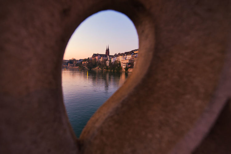 Buildings by river against clear sky at sunset seen through hole