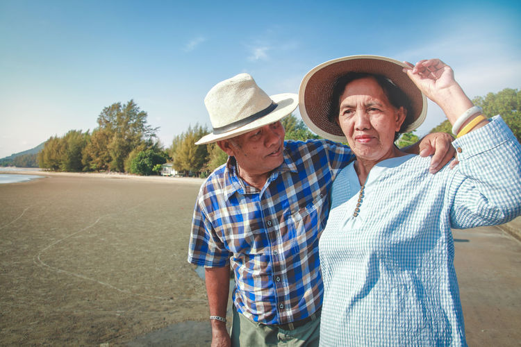 Senior couple standing at beach against sky