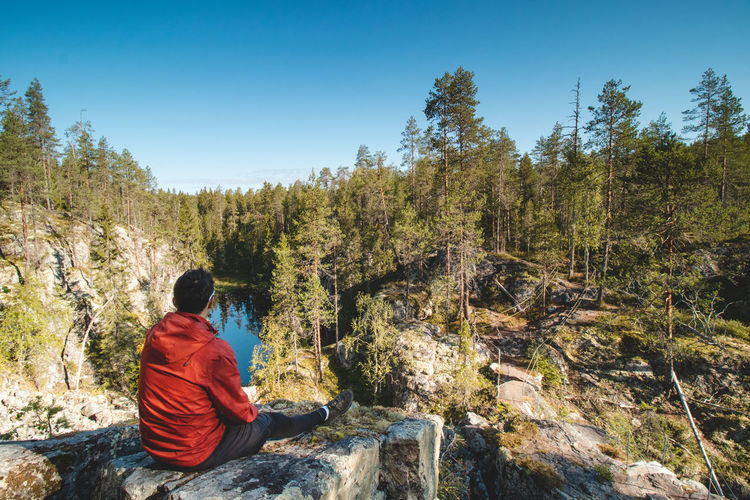 Traveller sits on rock and observes a beautiful natural lake in hiidenportti national park, sotkamo