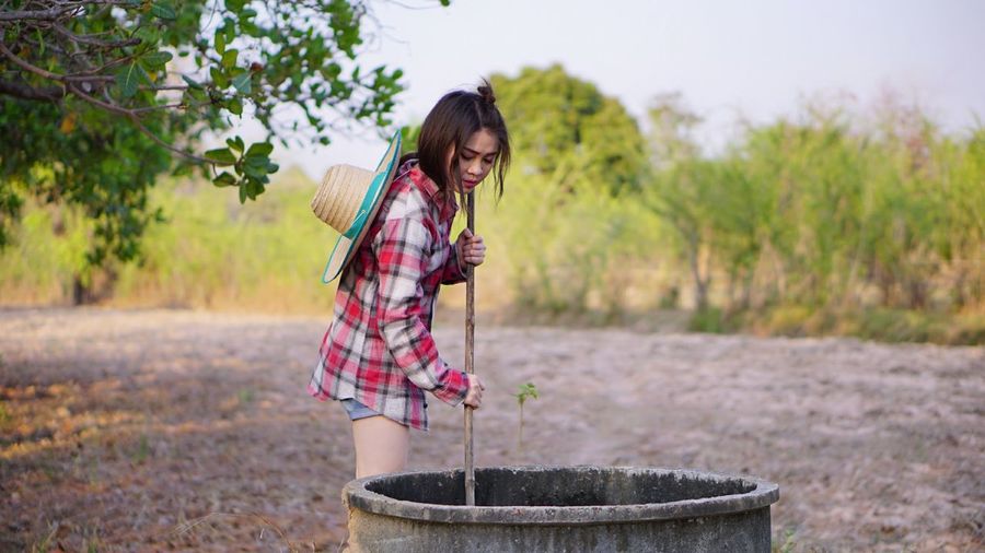 Young woman putting pole in well at farm