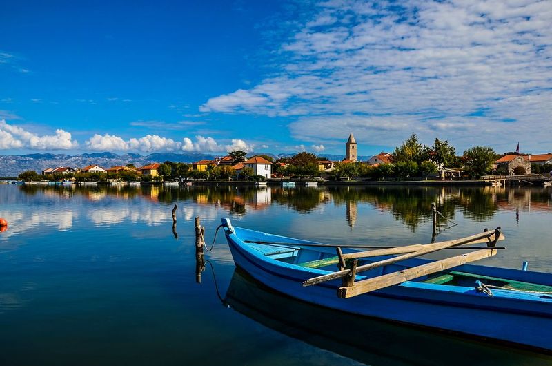 Boats moored in lake against blue sky
