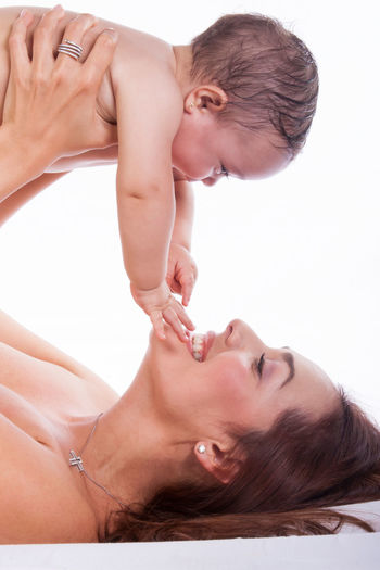 Happy mother playing with shirtless daughter while lifting her against white background