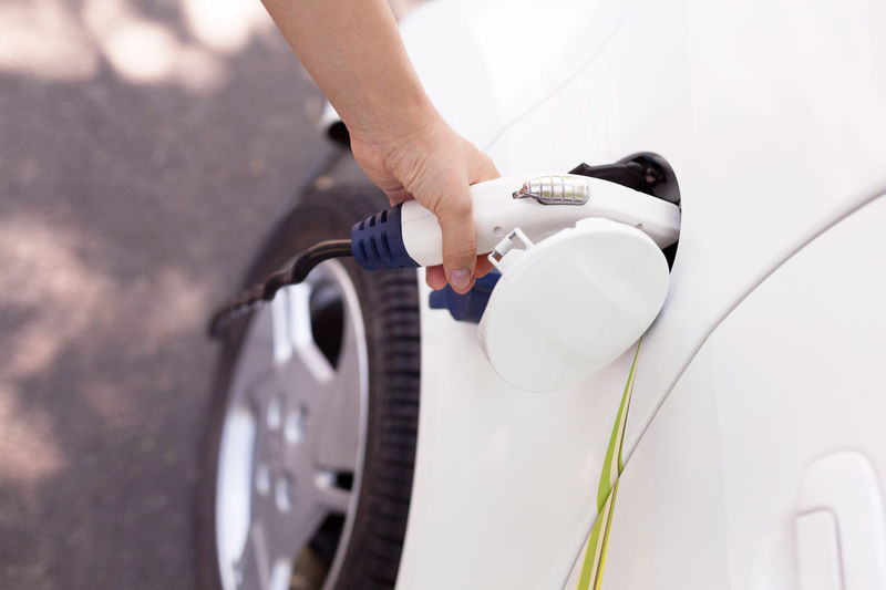 Cropped hand of woman charging electric car at station