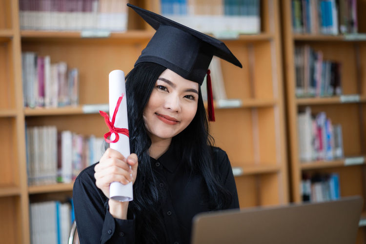 Portrait of student holding diploma at library