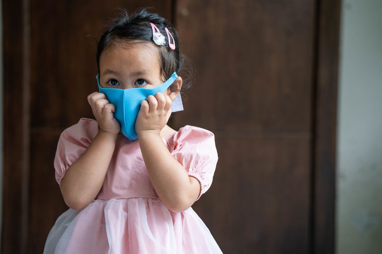 Cute little girl wearing healthy face mask to prevent virus and pm2.5 standing indoor.