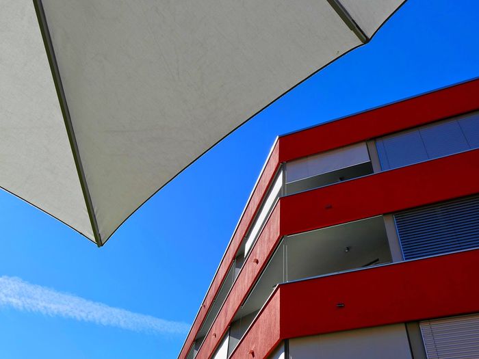 Low angle view of building and parasol against blue sky