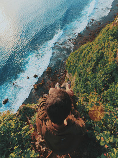 High angle view of man sitting on cliff by sea
