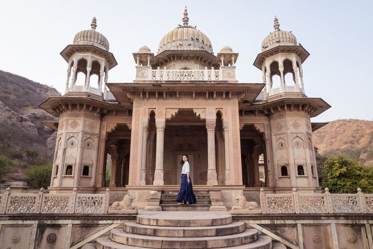 Side view of cheerful asian woman smiling and looking at camera while standing near aged gaitor ki chhatriyan building in jaipur, india