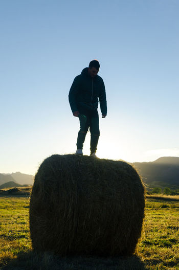 Man standing on top of hay bale looking down