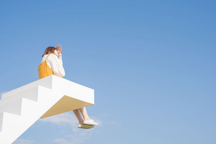 Low angle view of woman sitting against blue sky