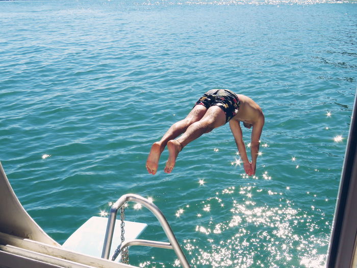 Rear view of man jumping in sea against sky
