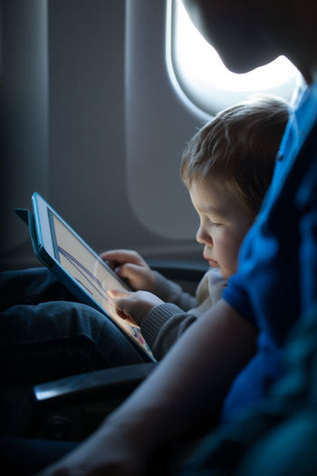 Cute boy using digital tablet while sitting in airplane