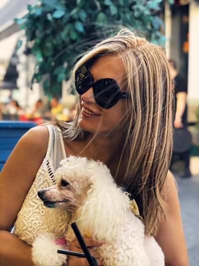 Smiling woman wearing sunglasses carrying dog in city