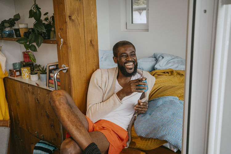 Happy mature man with coffee cup sitting with legs crossed at home