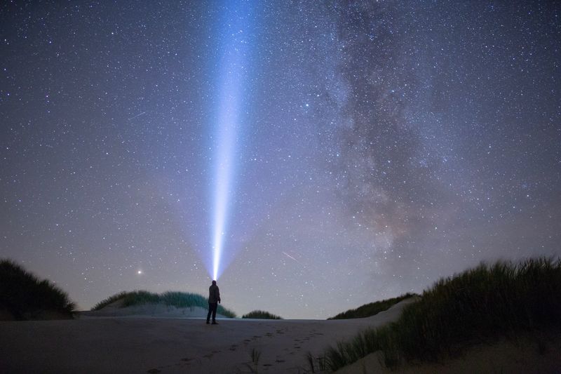 Man standing against sky at night with a flashlight. stars and milkyway above him. 