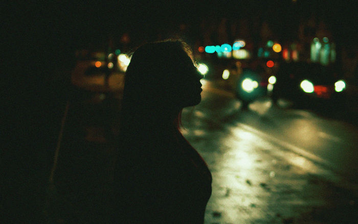 REAR VIEW OF WOMAN WALKING ON ILLUMINATED ROAD AT NIGHT