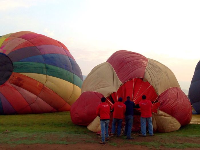 Men holding hot air balloon on field against sky