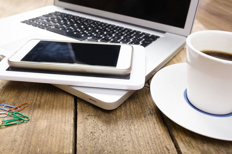Close-up of smart phone and laptop with coffee cup on table