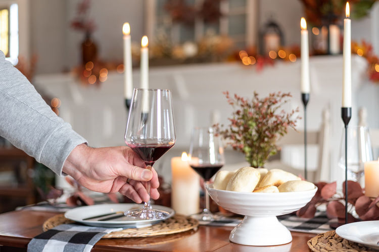 Man setting a glass of red wine on a festively decorated thanksgiving dining table 