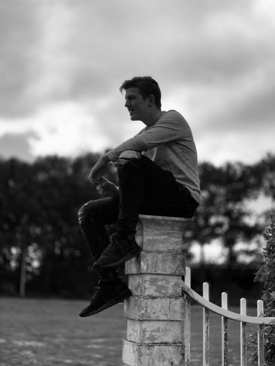 Side view of man sitting against sky