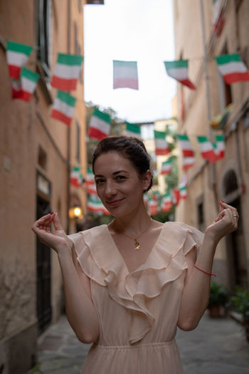 Portrait of woman smiling while standing against italian flags hanging amidst buildings
