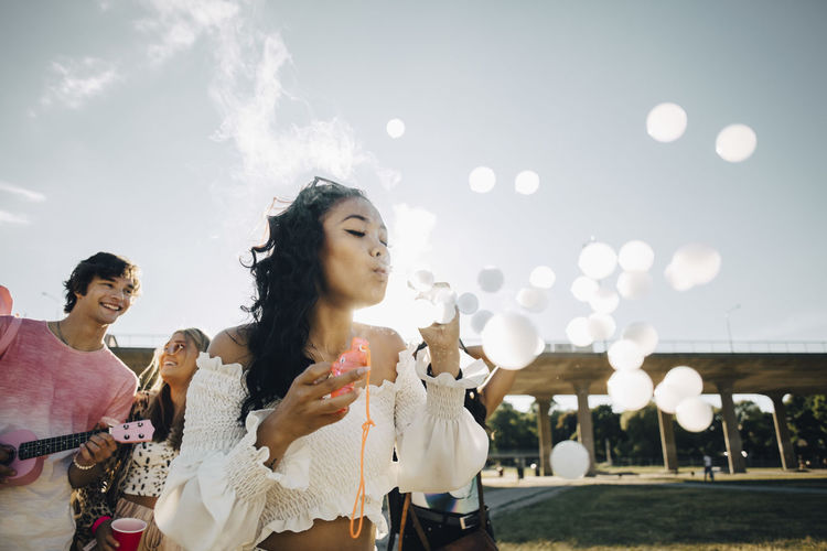 Young woman making smoke bubbles while enjoying with friends at music concert