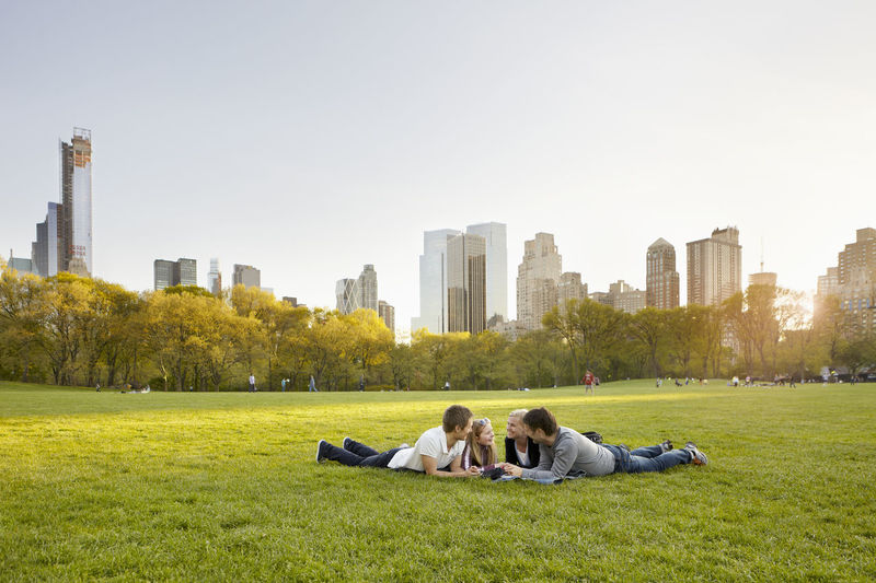 People relaxing on grass in city against sky