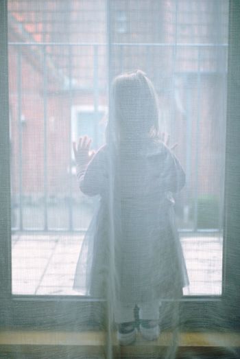 Rear view of girl looking through window at home