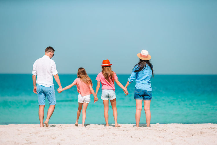 Rear view of family holding hands while standing on beach