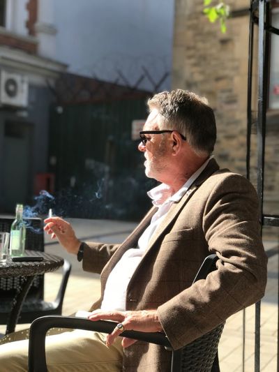 Side view of man smoking while sitting on table outdoors