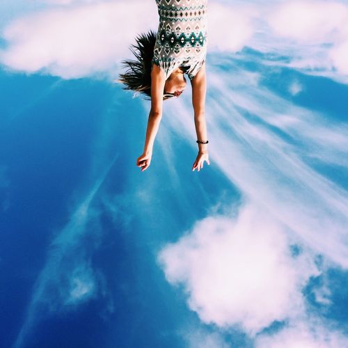 Upside down image of young woman with arms raised against sky