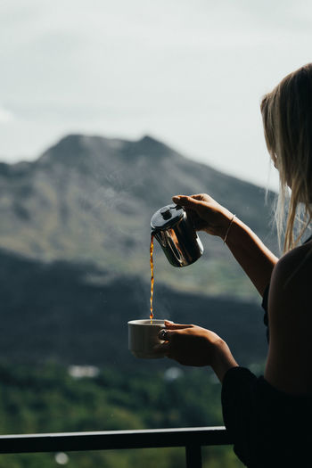 Woman pouring coffee in cup against mountain